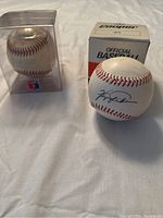 Two baseballs displayed side by side on a white sheet: one signed Ferguson Jenkins baseball, one game-used baseball with original box and display case.