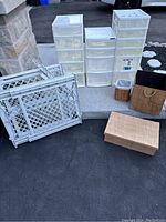 Complete lot of three plastic storage units, two baby gates, and three decorative boxes arranged on a concrete step and driveway.