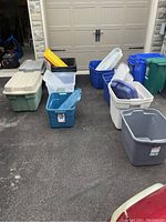 Photo showing various assorted plastic storage totes placed on driveway in multiple colors and sizes, some with lids and extra lids.