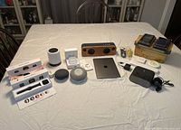 Overview of all electronics laid out on table showing speakers, smartwatches in boxes, iPad, earbuds, phone cases, humidifier, and Keurig coffee maker