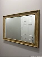 Wall mirror showing light wood frame and clear glass reflecting a door and wall.