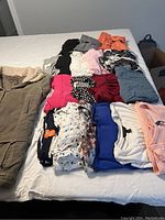 Photo shows neatly arranged women’s clothing on a bed including a mix of tops, shorts, pants, and a fall coat in various colors and prints.