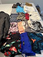 Clothes neatly arranged on bed, includes shorts, skirts, and blouses in various patterns and colors alongside a brown winter jacket.