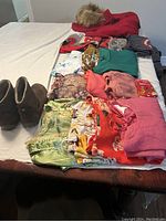 Full lot overview showing the red winter jacket, multiple folded tops and dresses, and brown boots on a white surface