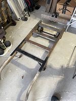 Side angle of an older wooden hand cart showing metal axle and two wooden handles with weathered wood
