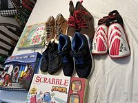 Photo showing three pairs of youth shoes, Mite shin guards, Scrabble Junior board game, and a Secret Decoder game set.