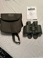 Binoculars, black carrying case, and instruction manual on white fabric surface