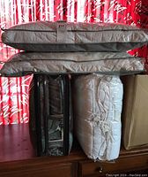 Stack of bedding items in sealed packaging including pillows, mattress cover, and bedding pieces.
