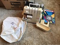 Overview of serger machine, cover, manual and guide book on carpet