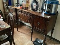 Photo of vintage wood buffet cabinet showing front view with three drawers, carved accents, and items on top.