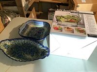 Two Polish ceramic serving dishes placed on a table in a basement. One is rectangular with scalloped edges and floral blue pattern, the other is square with blue pattern.