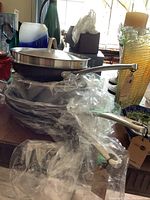 Stack of GreenPan cookware including frying pans with glass lids and handles, wrapped in plastic for protection.