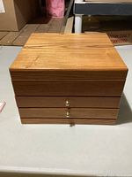 Closed wooden jewelry box with two drawers and gold-colored knobs on a white table.