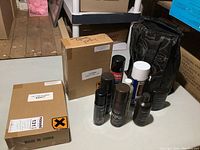 Two unopened cardboard boxes labeled as containing Precious Liquid Jewelry Cleaner and several leather care bottles and sprays on a white table surface with a carry bag.