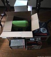 Open cardboard box containing green KitchenAid mixer and accessory boxes