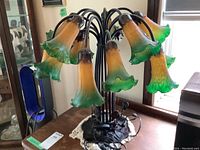 Full view of Tiffany style lily/tulip table lamp showing seven bell-shaped amber to green gradient glass shades and metal stem design.