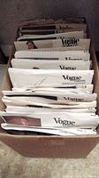 Box containing approximately 56 vintage Vogue sewing patterns showing front edges with various Vogue logos.