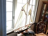 Model sailboat named "Bluenose" displayed near window on wooden stand, showing full length and rigging details.