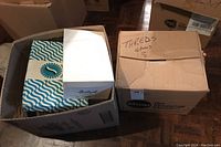 Two cardboard boxes; one open showing sewing buttons, ribbons, and spools of thread; the other closed labeled 'Threads & Pieces'