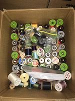 Box filled with assorted thread spools in multiple colors and sizes with some vintage labels.