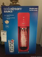 Front view of the SodaStream Source sparkling water maker box, showing product image and features including 3-level carbonation indicator and easy snap-lock bottle insertion.