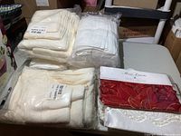 Overview photo showing packaged cream and white towels stacked beside a red packaged table runner and white linen on a table.