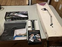 Full lot arranged on table showing all four boxed items: Magic Wand scanner, Avision MiWand 2 scanner, Belkin laptop cooling pad, clamp-on magnifier lamp.