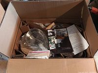 Open cardboard box showing cookware pieces wrapped in plastic and packed in compartments