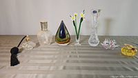 Full image showing all seven items on table including perfume bottle, Berger lamp, glass drop, daisies, Bohemia vase, crystal lily, and glass pumpkin