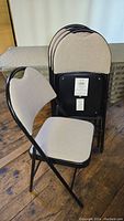 Four light gray fabric padded folding chairs with black metal frames, one chair set up facing camera and three stacked behind it.