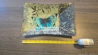 Top-down view of glass plate showing butterfly and gold floral decorations alongside a measuring tape indicating plate length of approximately 11.5 inches.
