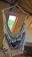 Hammock swing seat hanging from wooden crossbar with blue, white, and red stripes and white fringes, shown indoors.