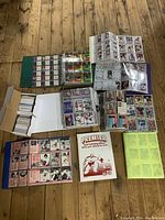 Overview of the entire hockey card collection, including several binders filled with cards, boxes of loose cards, and a Premier card collecting album on a wooden floor.