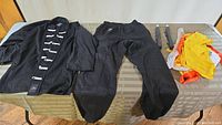 Black Kung Fu gi jacket, pants, foam sticks, and assorted sashes laid out on a table.