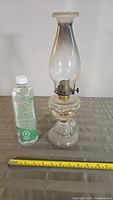 Full view of vintage glass oil lamp standing 15.5 inches tall next to bottle of lamp oil and measuring tape