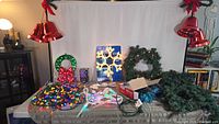 Photo showing all outdoor Christmas items on table including multi colored LED lights, wreaths, garlands, bells, and storage tote