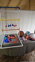 Full lot showing ladder toss game with bolas hanging, basketball, volleyball, multiple frisbees, shuttlecocks, hand air pump, and catapult on table.