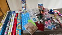 View of entire collection of party supplies, including gift wrapping rolls, ribbons, bows, and party banners on table.
