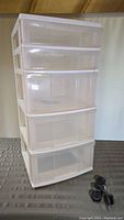 Full view of five-drawer plastic storage unit showing translucent drawers and white frame, with wheels detached in foreground.