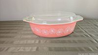Full shot of the pink oval Pyrex casserole dish with white daisy print and clear glass lid on top.