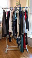 Photo of assorted women's clothing hanging on rack, showing variety of garments including coats, blazers, dresses and cardigans.