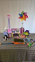 Photo showing an assortment of youth-oriented items on a table including a garden windmill, bubble wand and machine, butterfly decor, boogie board, magnetic cat paw gloves, plush toy, and other small toys and packages