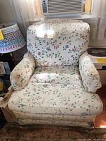 Frontal view of a floral upholstered armchair, showing the cushioned back, seat, and armrests with visible wear on the fabric.
