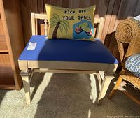 Front view of wooden bench with blue seat cushion and decorative yellow throw pillow with palm tree and flip-flops design