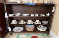 Front view of wooden bookcase with various dishes on shelves, showing overall condition and size.
