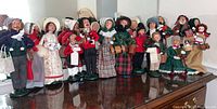 Seventeen Byers Carolers figurines lined up on a wooden surface showing variety of sizes, clothing, and accessories.