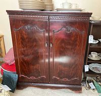 Full view of the cabinet front showing ornate carved details on doors and top edge, dark wood finish, surface wear and scratches.