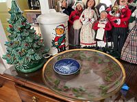 Photo showing the green ceramic light-up Christmas tree, white ceramic cookie jar with bear design, hand painted glass platter with holly and berries, and small commemorative plate, displayed with Christmas caroler figurines in background.