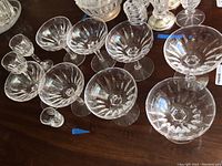 11 pieces of clear crystal stemware displayed on wooden table, showing geometric cut glass patterns and various stem styles.
