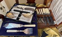 Boxed serving spoons and matching knife and fork set with ivory-colored handles, laid out on a chair